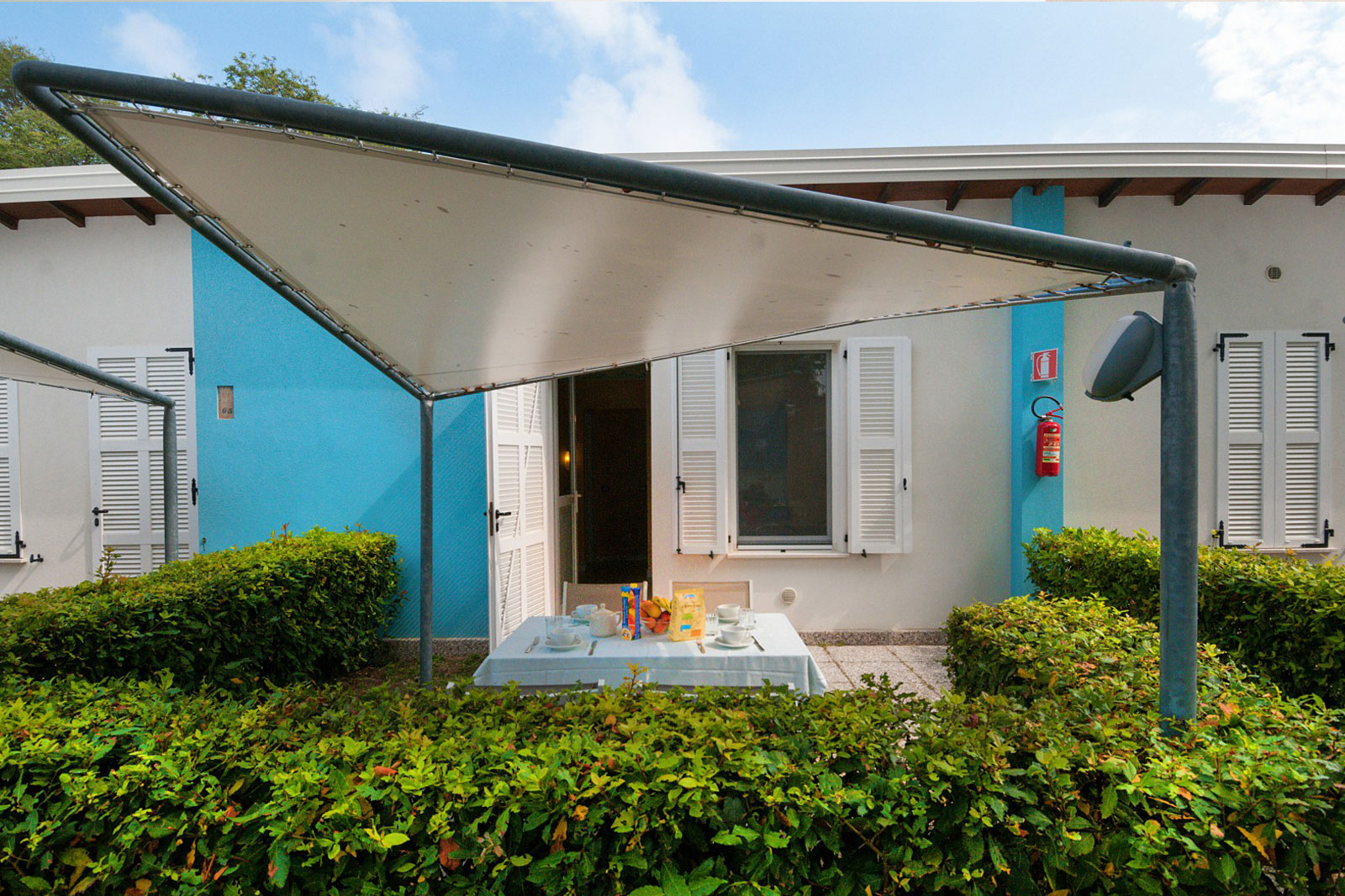 Patio coperto del Bungalow Mare con tavolo per la colazione, circondato dal verde al Park Gallanti Holiday Village